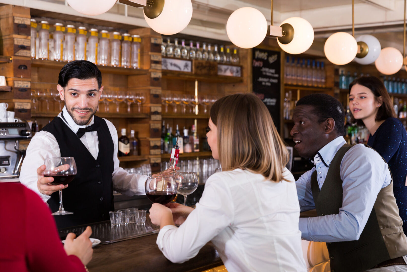 Young people are relaxing near bar counter and drinking alcohol Bartender serving drinks to customers at bar.