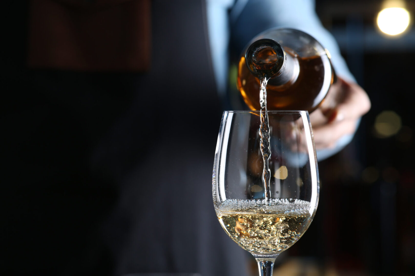 Bartender pouring white wine from bottle into glass indoors, closeup. Space for text Pouring white wine into a glass.
