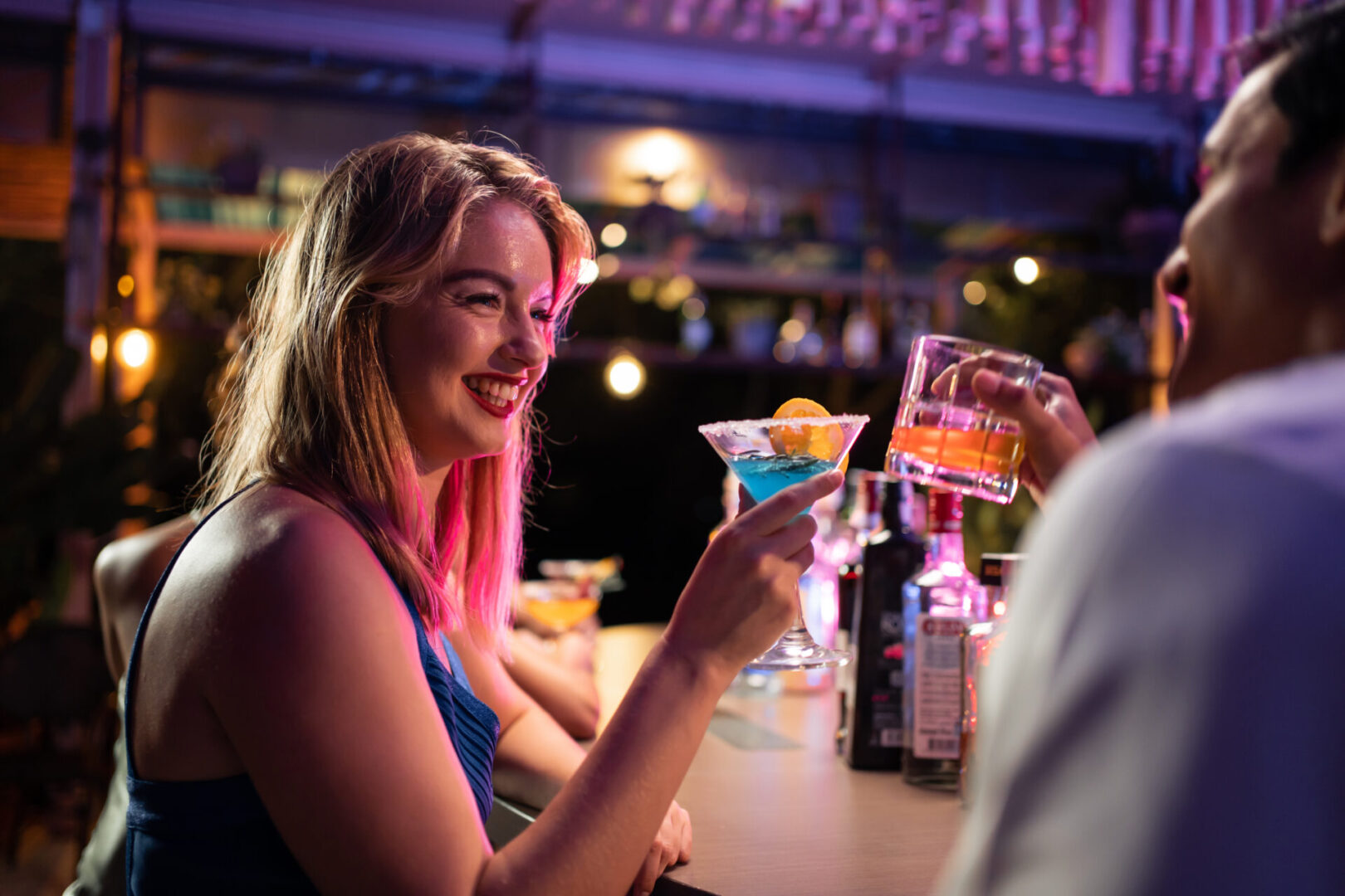 Beautiful young couple having fun, drinking alcohol cocktail in a bar. Attractive friend man and woman feeling happy and relax having a party, drink a glass of beer to celebrating event at night club. People enjoying drinks at a bar.