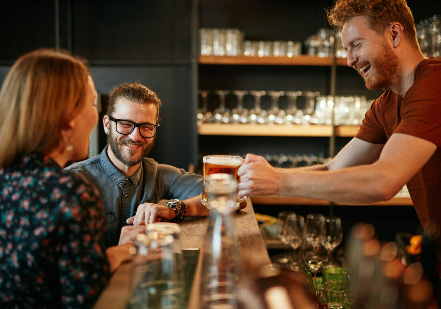 Bartender serving beer to customers. Pub interior. Bartender serving drinks to two customers smiling.