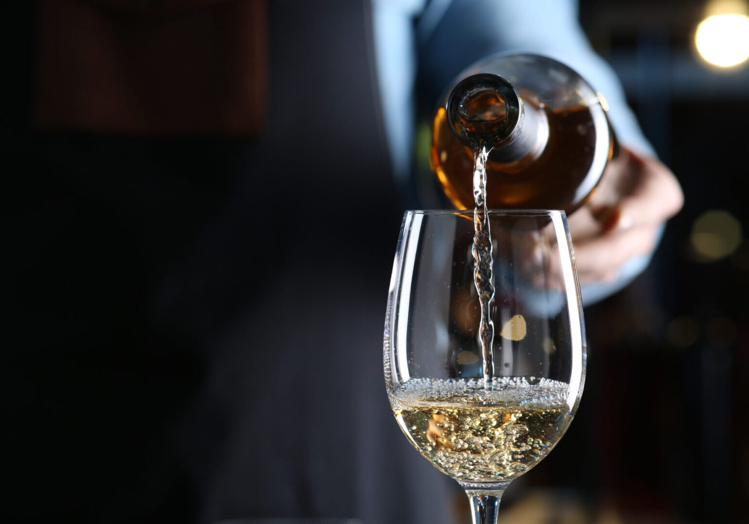 Bartender pouring white wine from bottle into glass indoors, closeup. Space for text Pouring white wine into a glass.