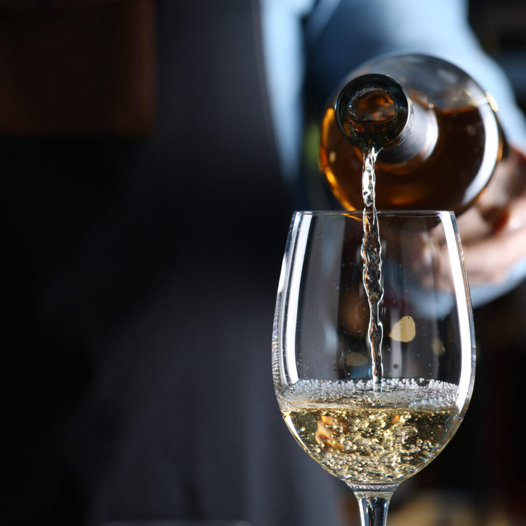 Bartender pouring white wine from bottle into glass indoors, closeup. Space for text Pouring white wine into a glass.