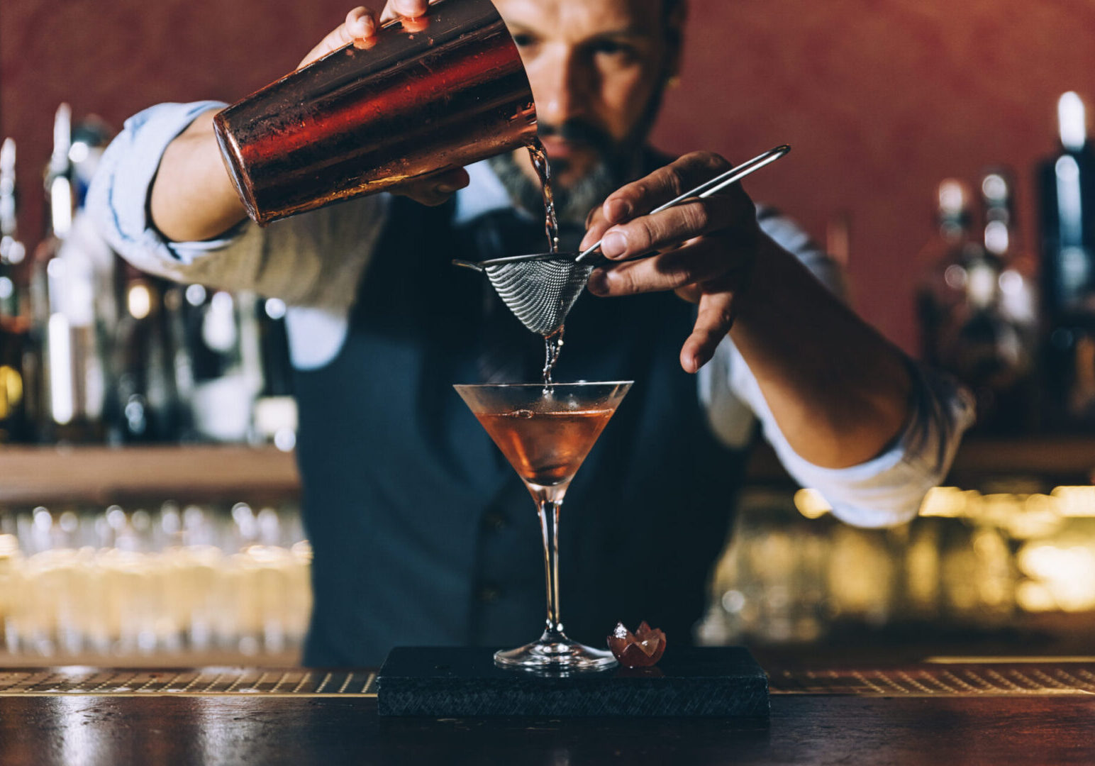 Barman is making cocktail at night club. Bartender pouring cocktail into a martini glass.